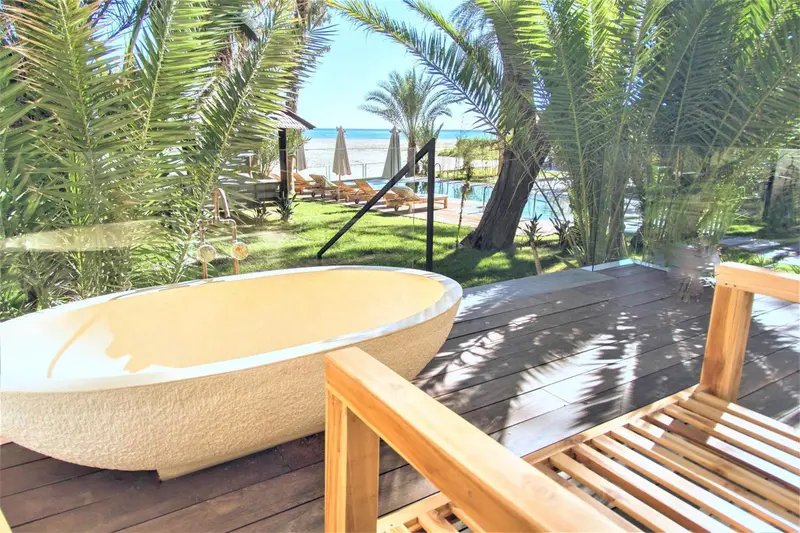 Baignoire extérieure sur une terrasse en bois avec vue sur une piscine et la mer.