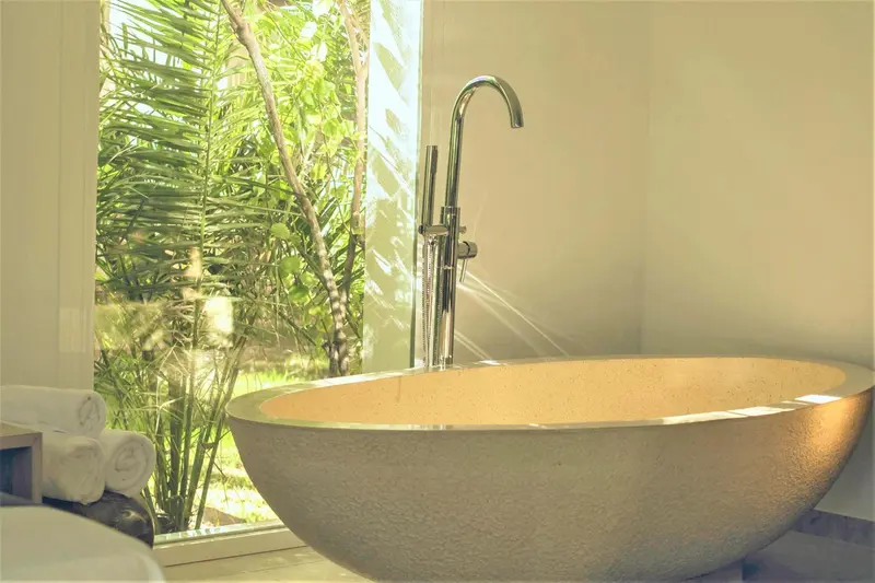 Une baignoire moderne est placée devant une grande fenêtre ouverte sur la végétation.