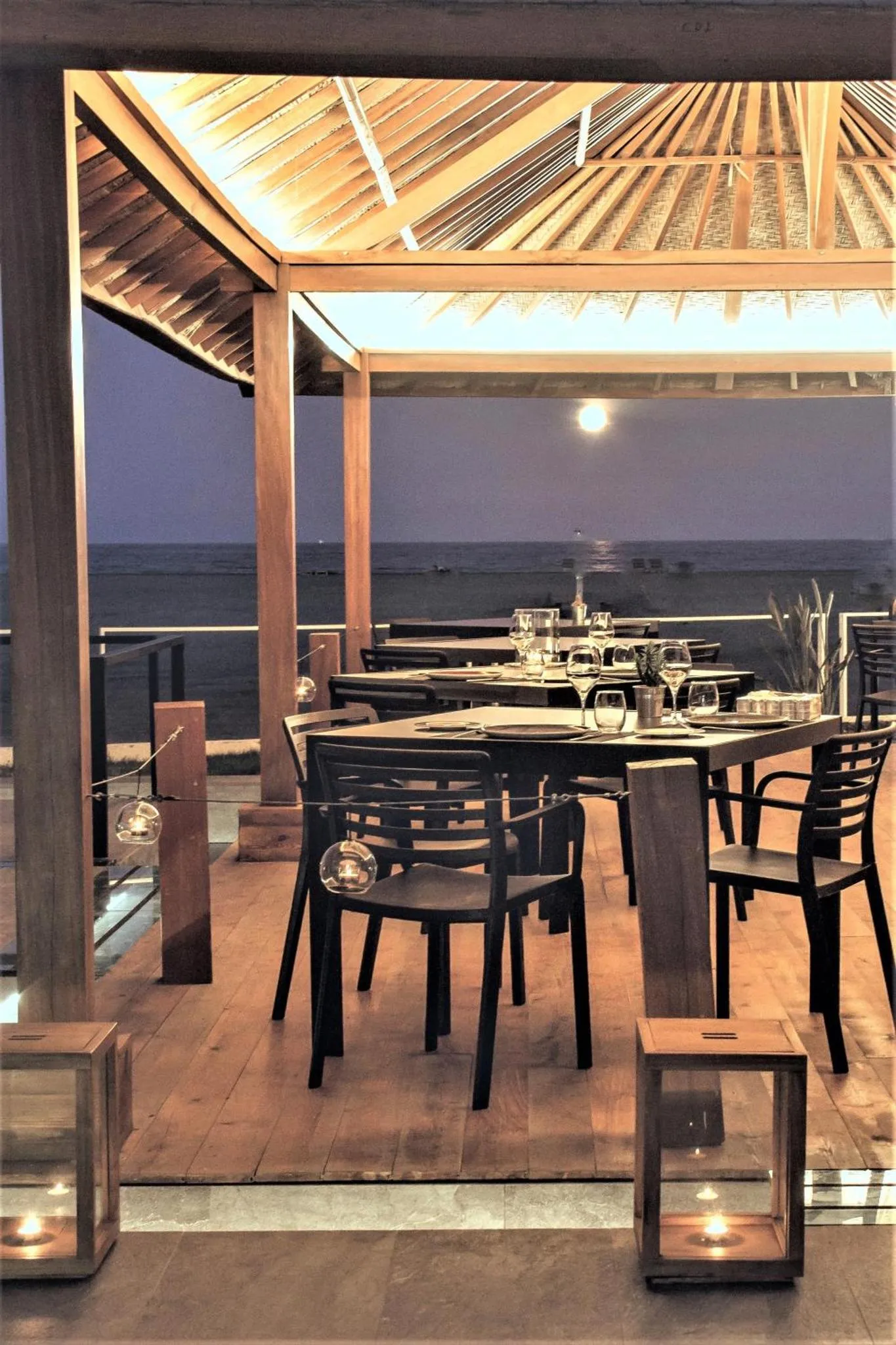 Une table est dressée sur une terrasse en bois avec une vue sur la mer au crépuscule.