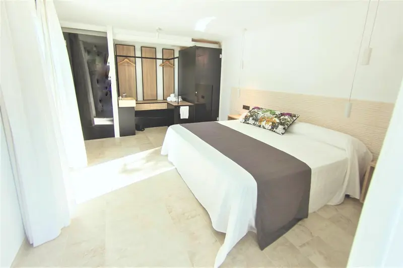 Une chambre lumineuse avec un grand lit recouvert d'une courtepointe blanche et grise.