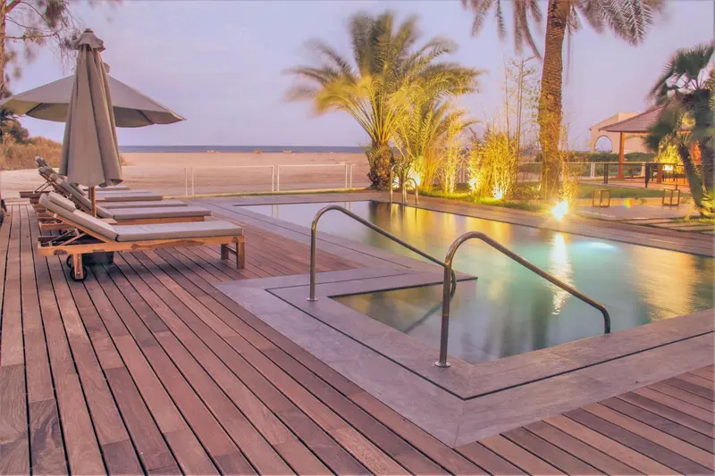 Terrasse en bois avec piscine et transats au coucher du soleil.