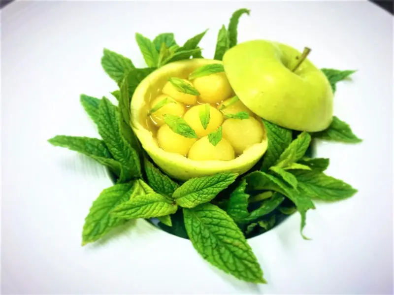 Une composition de fruits frais et de menthe est présentée sur une assiette blanche.