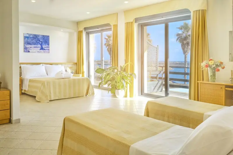 Chambre lumineuse avec lits et vue sur la mer par de grandes baies vitrées.