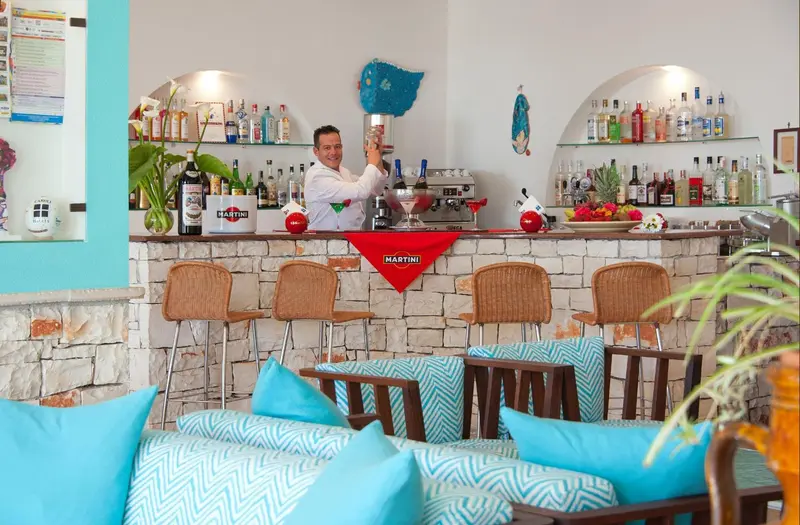 Un barman prépare une boisson derrière un comptoir décoré de bouteilles.