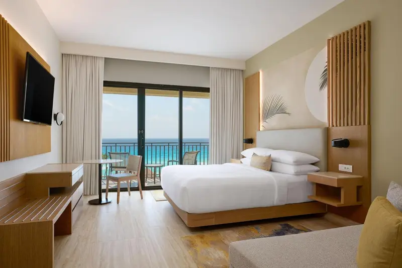 Chambre lumineuse avec un grand lit et une vue sur la mer depuis un balcon.