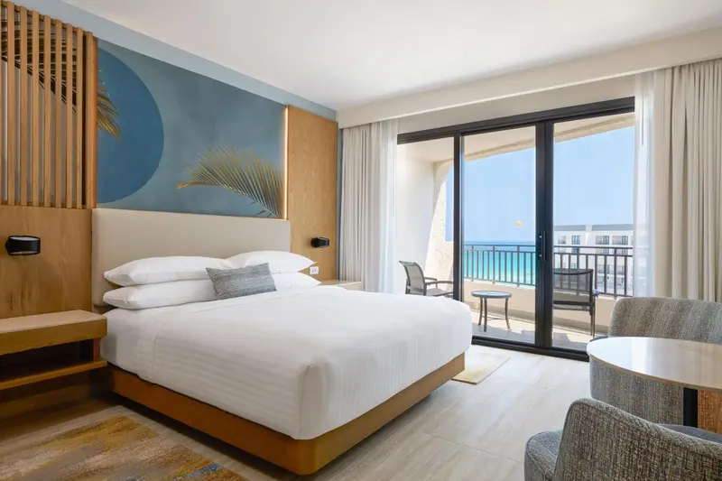 Une chambre lumineuse avec un grand lit et un balcon donnant sur la mer.