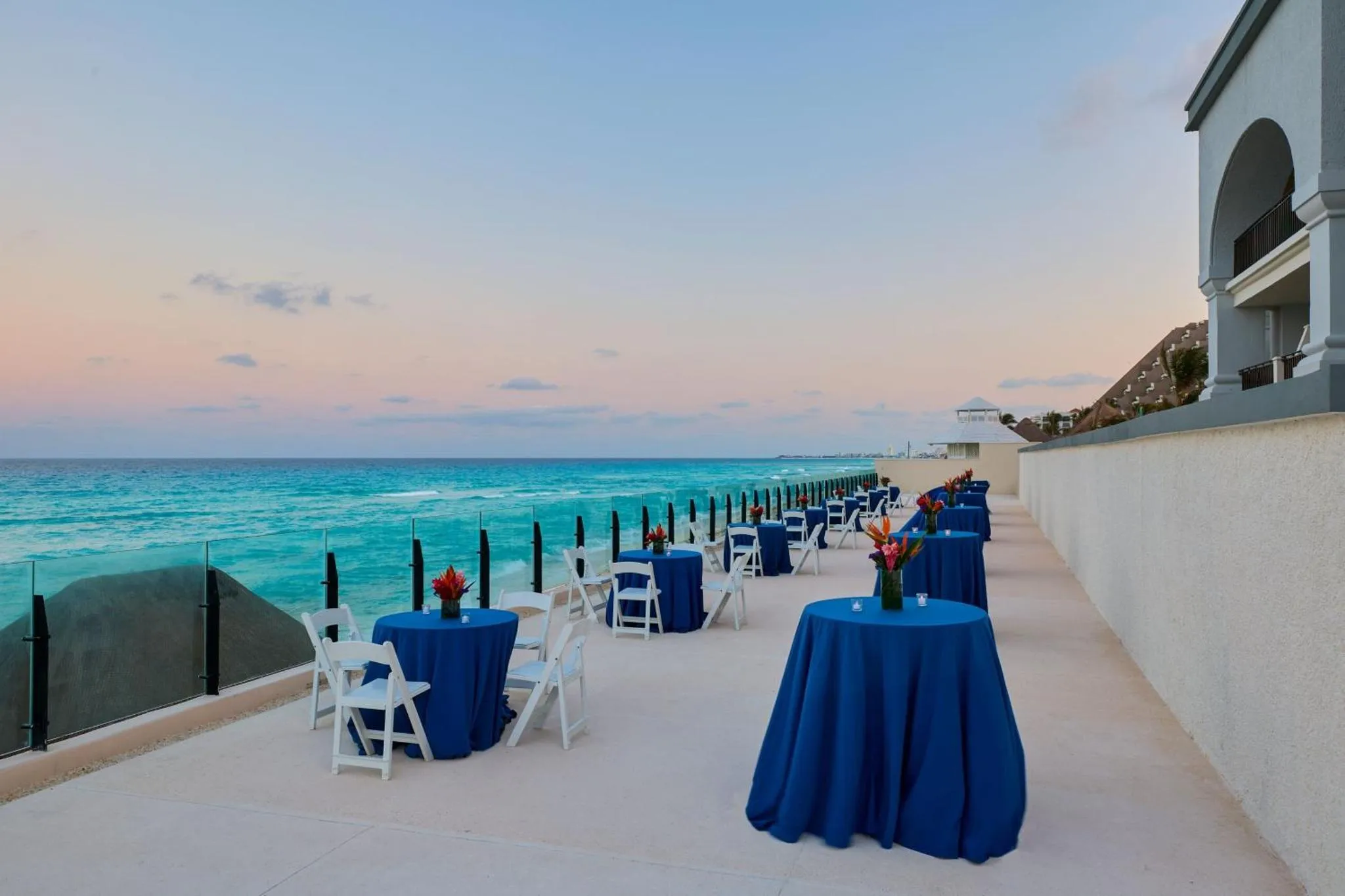 Terrasse avec tables et chaises face à la mer au crépuscule.