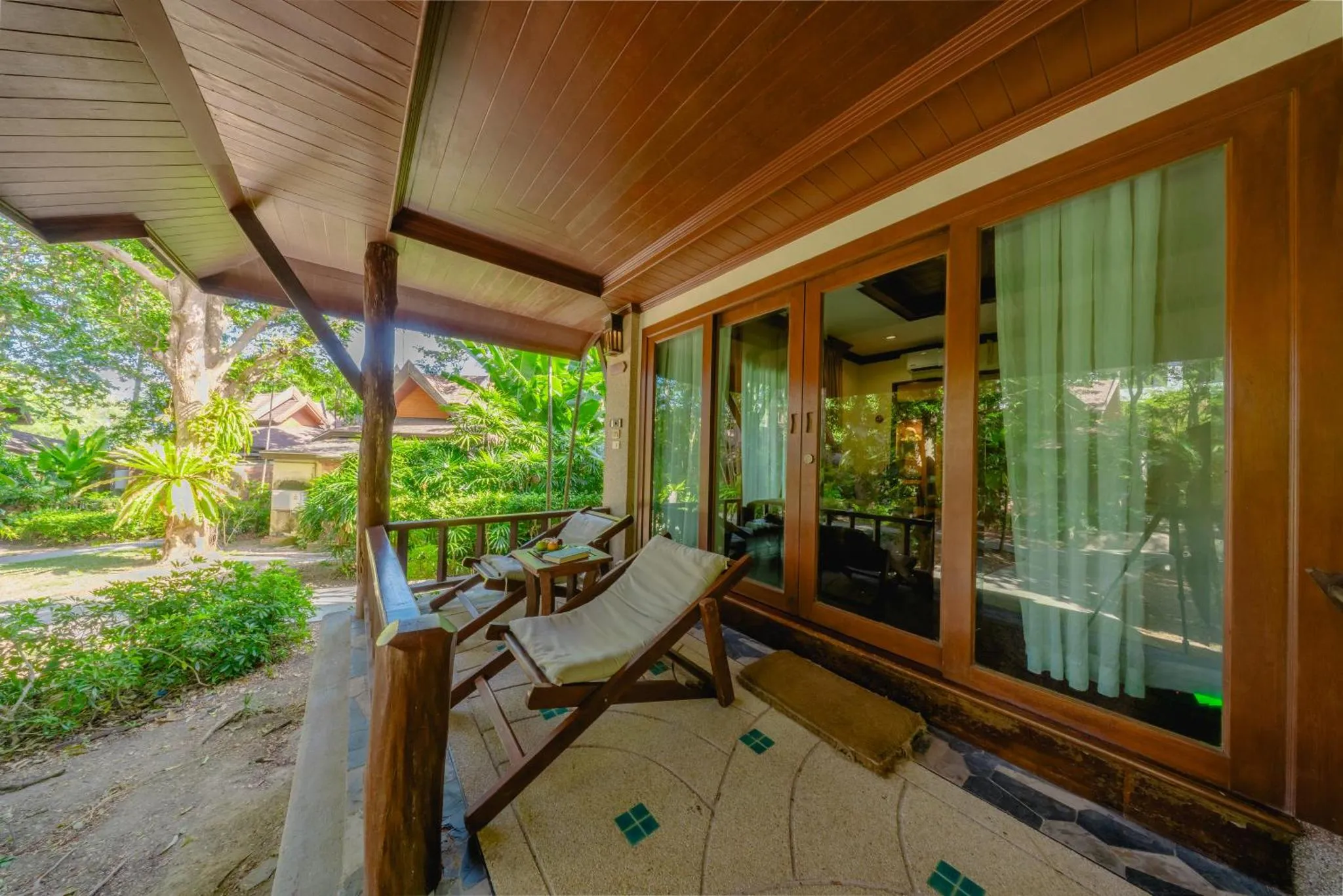 Terrasse ombragée avec mobilier de détente donnant sur un jardin tropical.