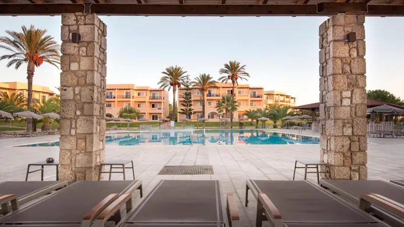 Transats alignés devant une piscine et un bâtiment à plusieurs étages.