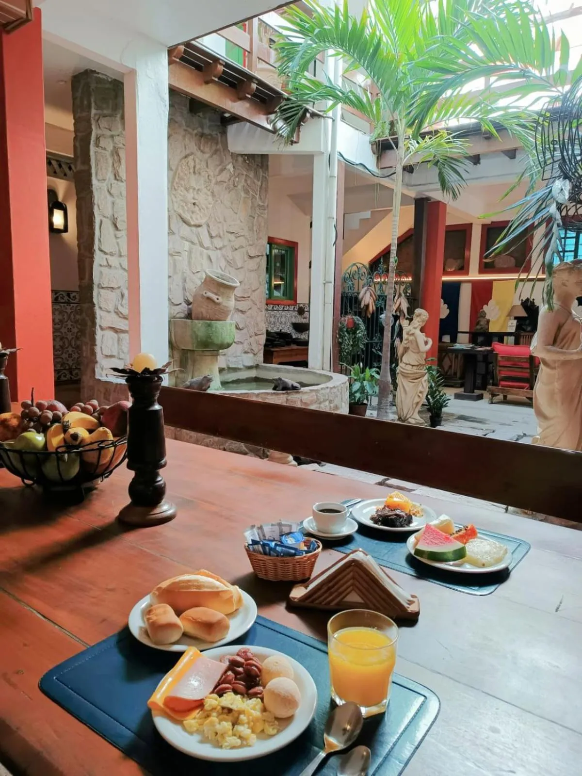 Une table est dressée avec un petit-déjeuner composé de fruits, de viennoiseries et de boissons.