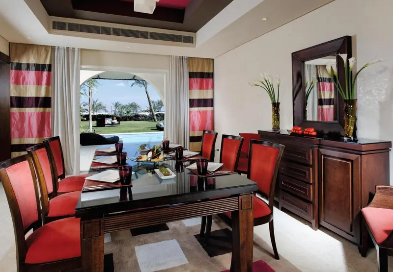 Une table à manger est dressée dans une salle lumineuse avec vue sur une piscine et un jardin.