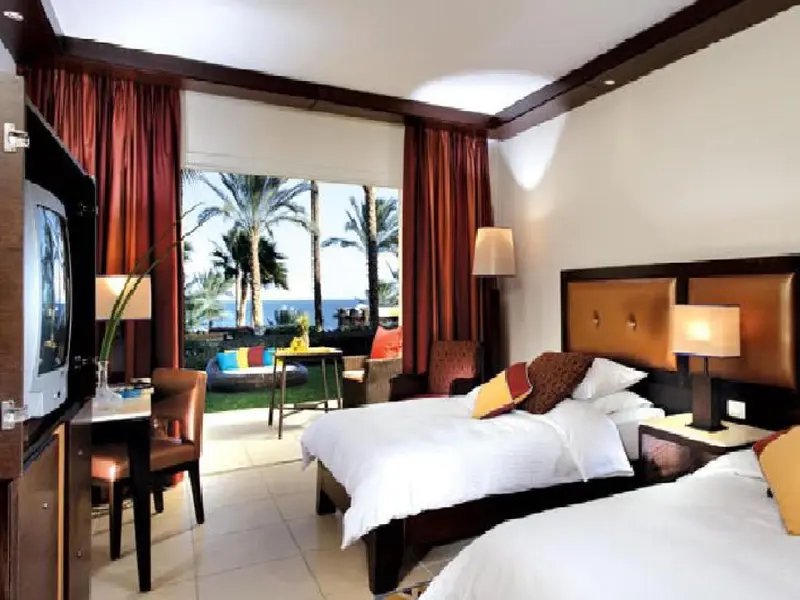 Chambre lumineuse avec lits jumeaux et vue sur la végétation et la mer.