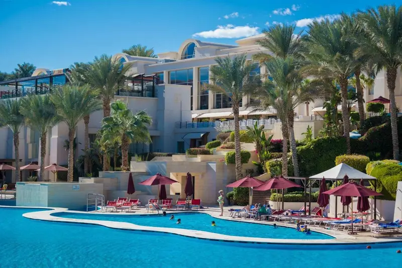 Bâtiment blanc entouré de végétation tropicale avec une piscine au premier plan.