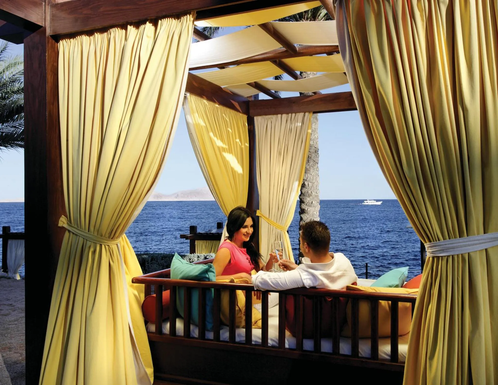 Un couple se détend sur un canapé dans une structure ombragée face à la mer.