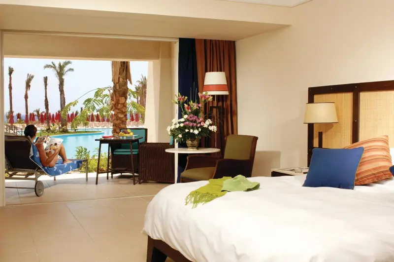 Une chambre lumineuse s'ouvre sur une terrasse avec vue sur une piscine et une végétation tropicale.