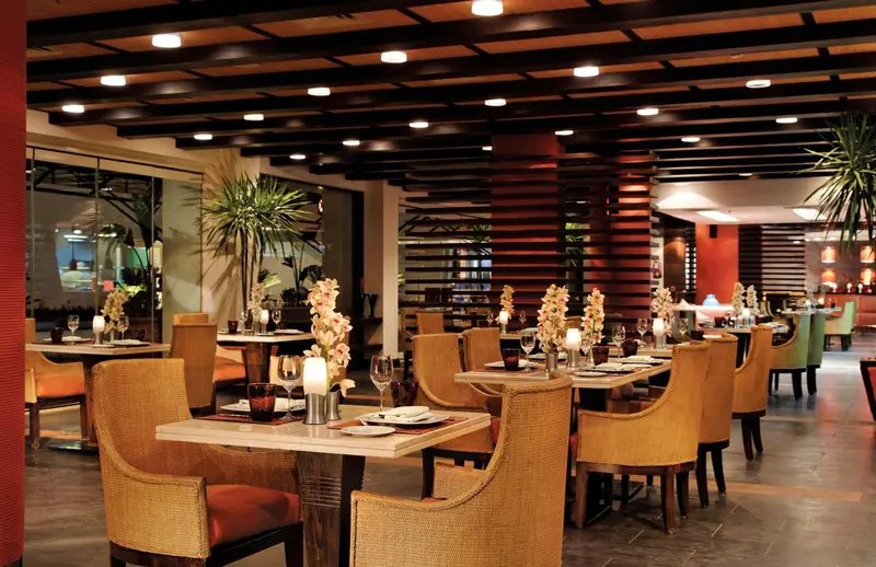Une salle de restaurant lumineuse avec des tables dressées et des chaises en rotin.