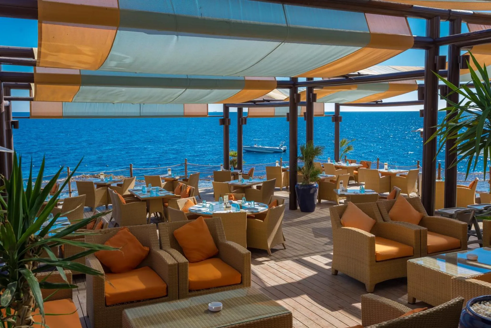 Terrasse ombragée avec mobilier de détente et tables de repas face à la mer.