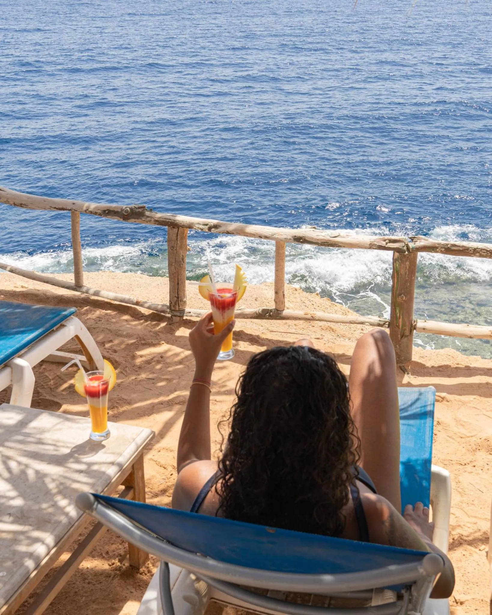Une personne se détend sur une chaise longue avec un cocktail face à la mer.