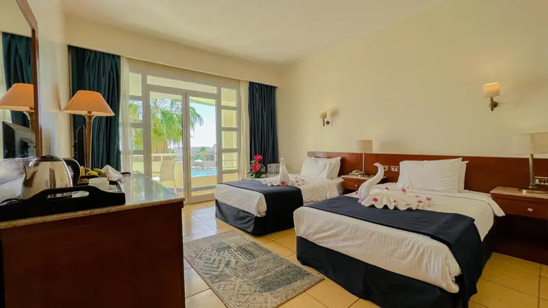 Chambre lumineuse avec deux lits simples et vue sur une piscine.