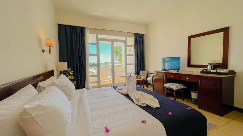 Chambre lumineuse avec un grand lit et une vue sur l'extérieur.