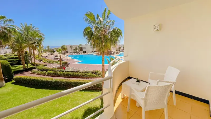 Vue d'un balcon avec mobilier blanc donnant sur une piscine et un jardin tropical.