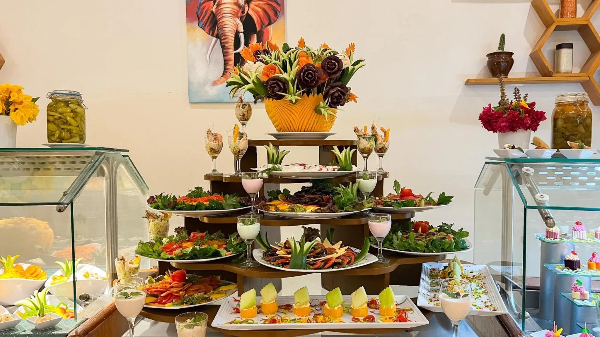 Présentation soignée de salades et de fruits sculptés sur un buffet.