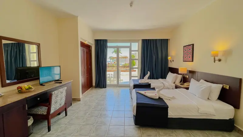 Chambre lumineuse avec deux lits et vue sur la mer par une baie vitrée.