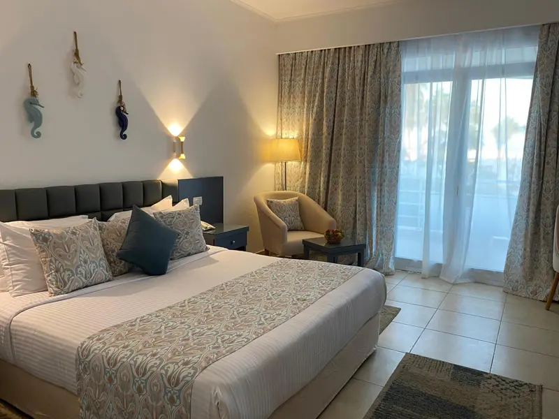 Une chambre lumineuse avec un grand lit et un fauteuil près d'une baie vitrée.