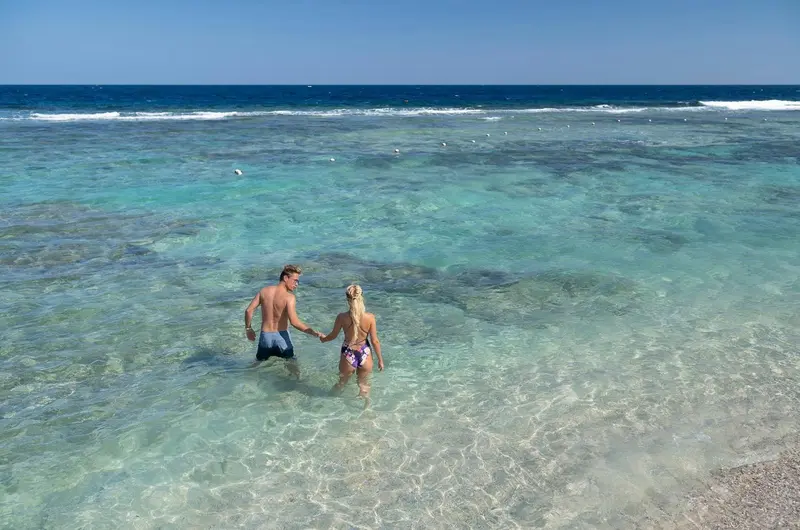 Un couple marche dans une eau turquoise peu profonde.