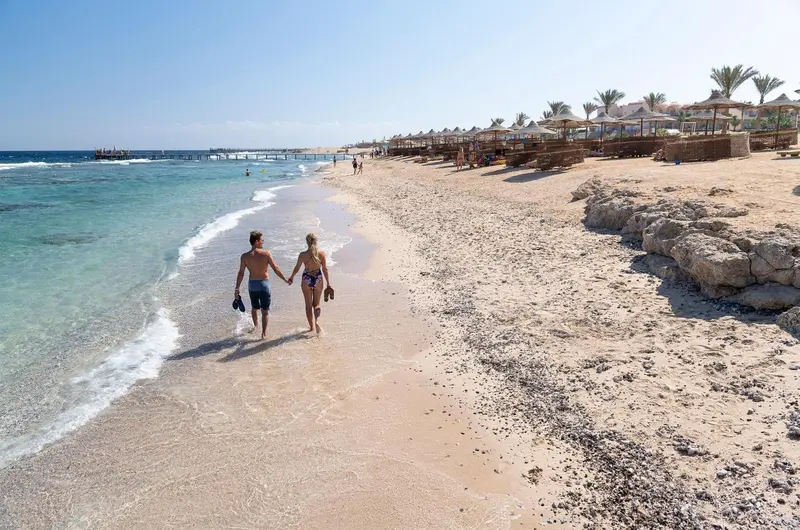 Un couple se promène sur une plage de sable fin au bord d'une mer turquoise.