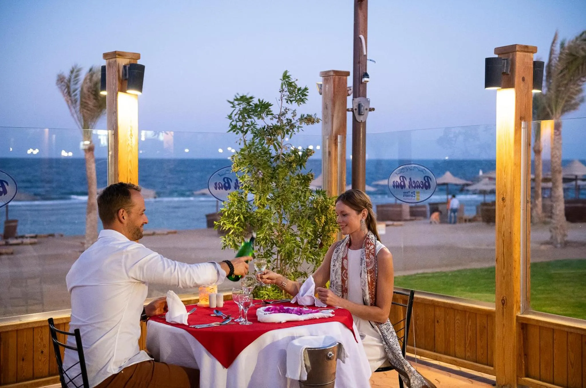 Un couple dîne à une table décorée en extérieur, face à la mer.