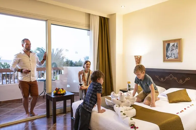 Une famille se trouve dans une chambre d'hôtel lumineuse avec un balcon.