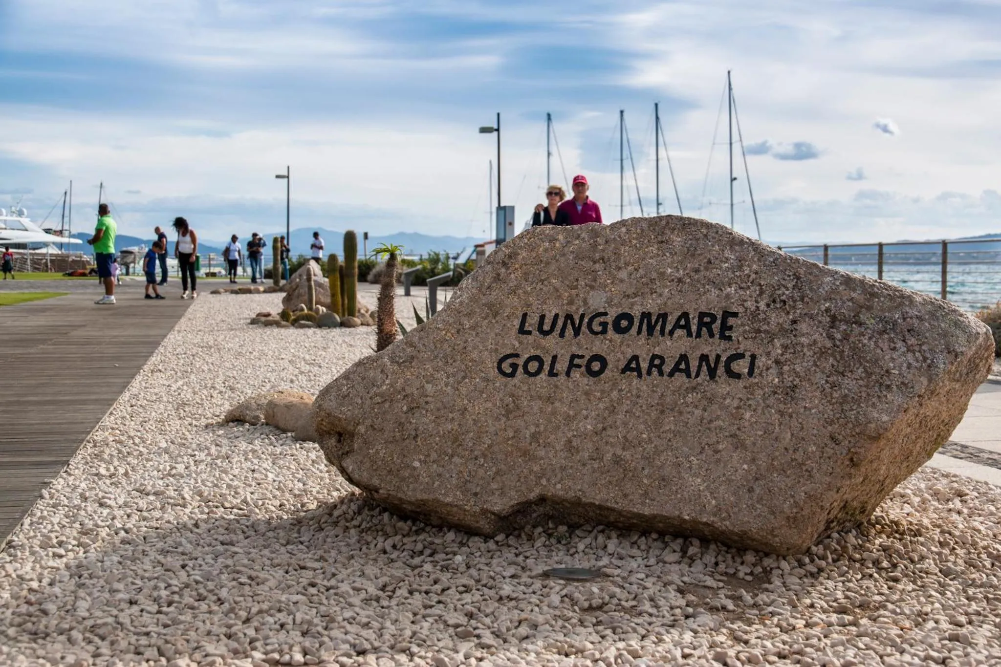 Une promenade en bord de mer avec une grande roche gravée d'un nom de lieu.