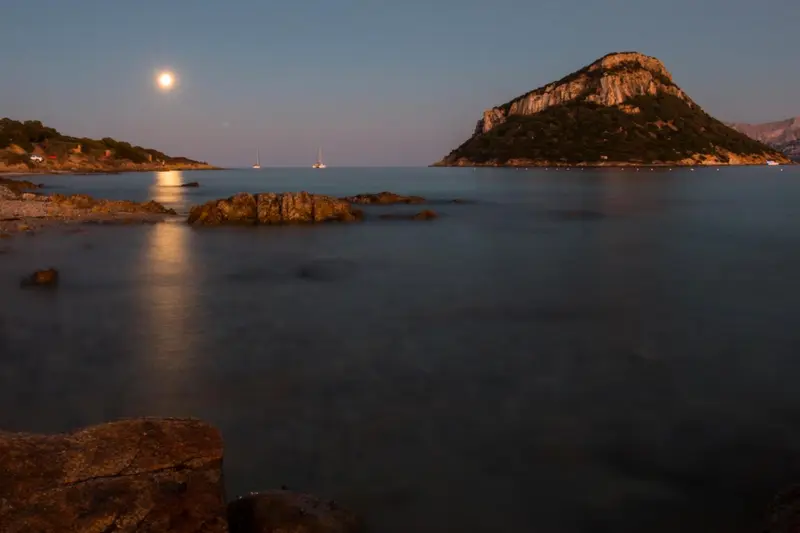 Paysage côtier avec une colline rocheuse illuminée par la lune.