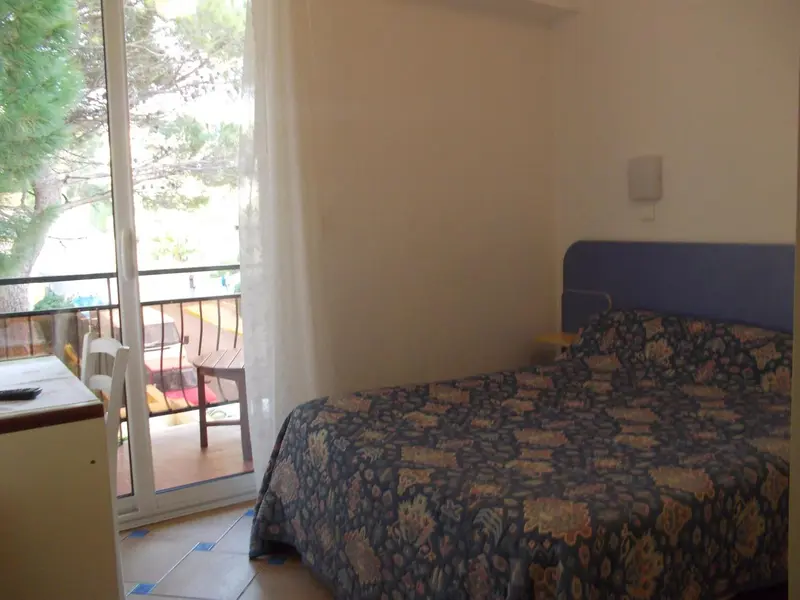 Une chambre lumineuse s'ouvre sur une terrasse avec vue sur la végétation.