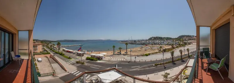 Vue panoramique sur la mer et la ville depuis un balcon.