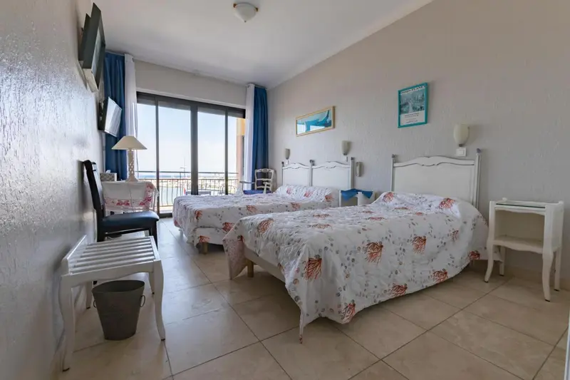 Chambre lumineuse avec deux lits simples et vue sur la mer.