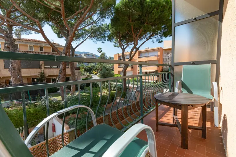 Une terrasse avec mobilier de jardin offre une vue sur la végétation et des bâtiments.