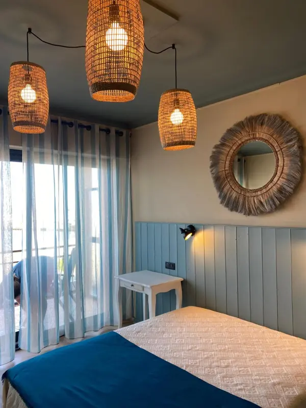 Une chambre lumineuse avec un lit recouvert d'une couverture bleue et des luminaires en rotin.
