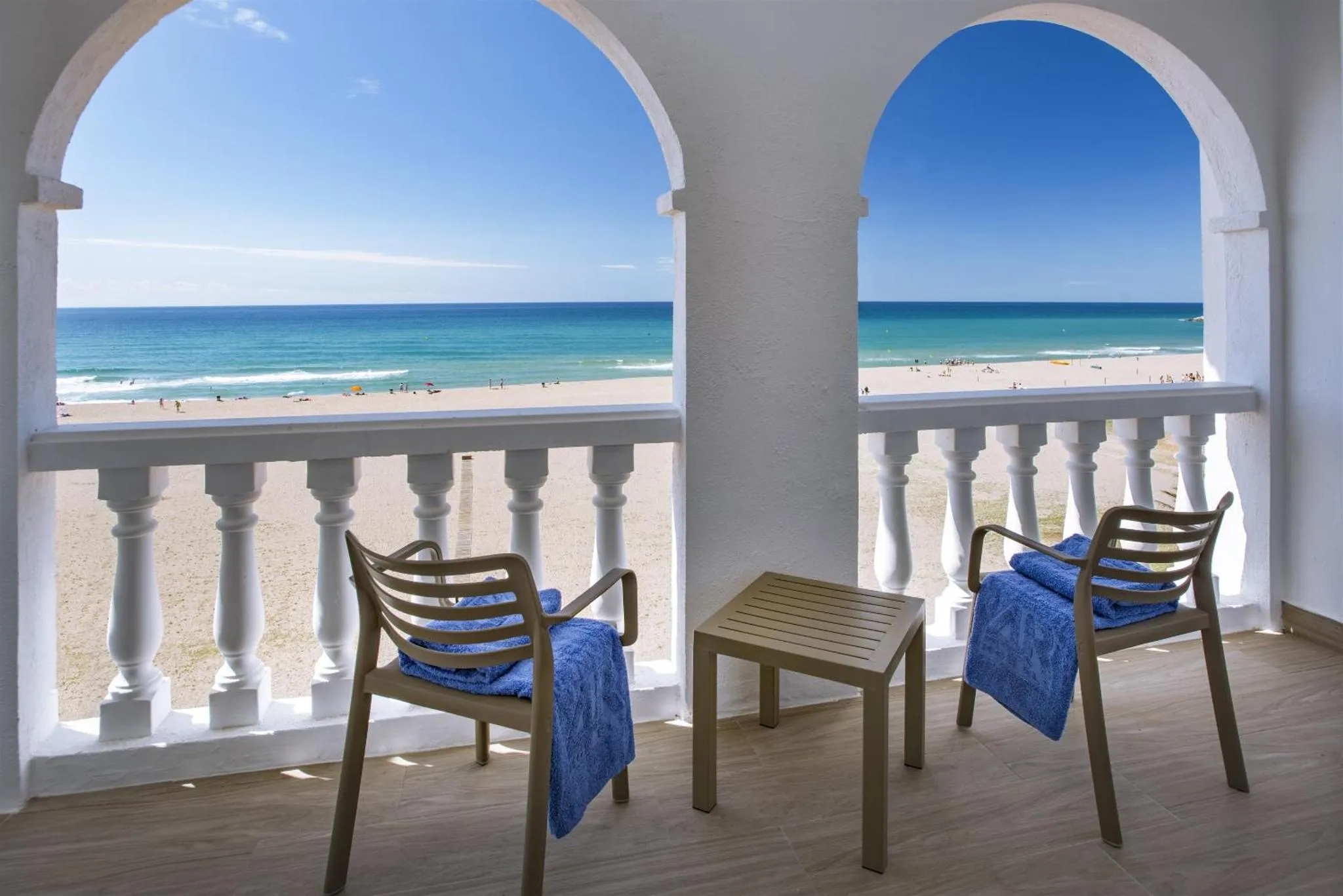 Deux fauteuils et une table basse sur une terrasse avec vue sur la mer et la plage.