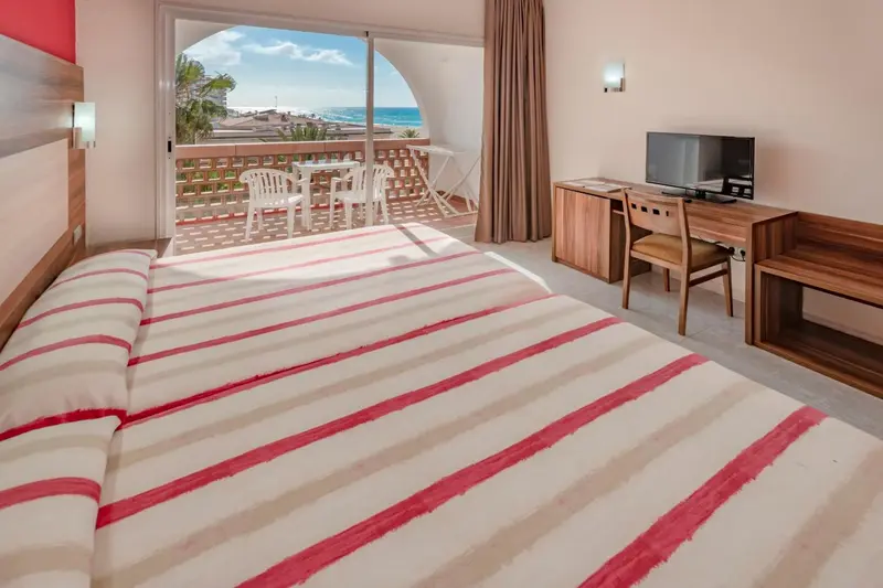 Une chambre lumineuse avec un grand lit donnant sur une terrasse et la mer.