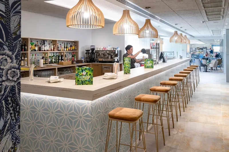 Un comptoir de bar moderne avec des tabourets et une personne qui prépare des boissons.