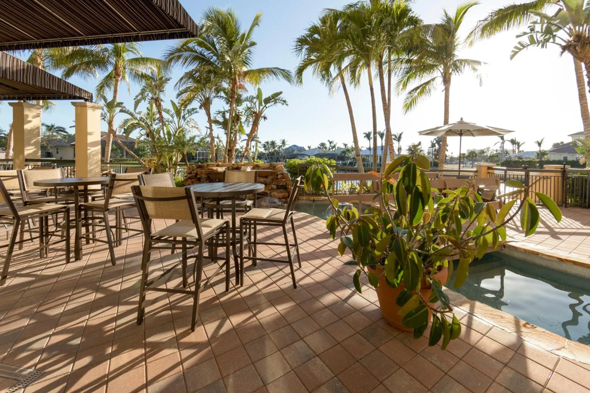 Terrasse ombragée avec tables et chaises près d'une piscine.