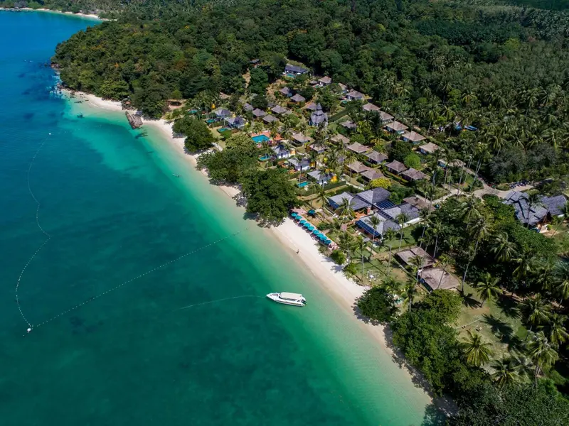 Vue aérienne d'une plage bordée de végétation et de bâtiments.