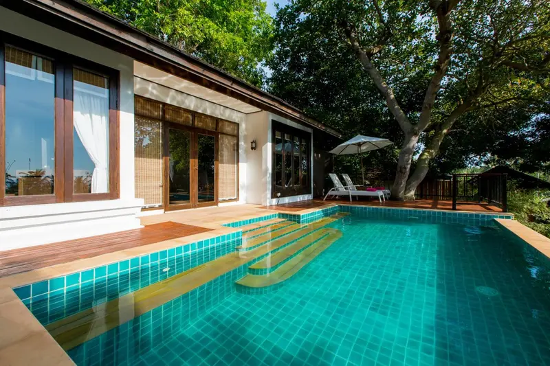 Une piscine turquoise est bordée d'une terrasse en bois avec des chaises longues.