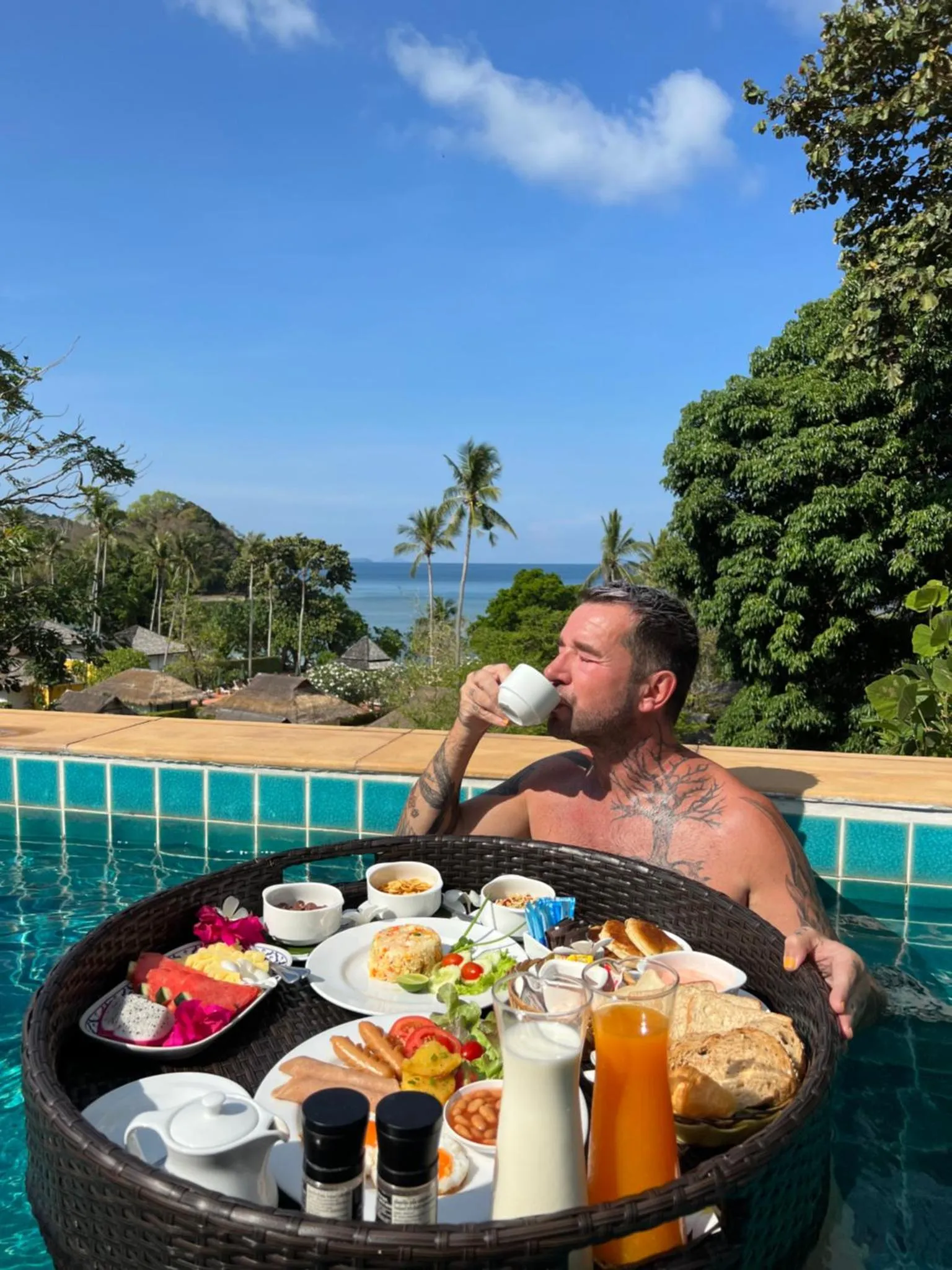 Un homme déguste un copieux petit-déjeuner sur un plateau flottant dans une piscine avec vue sur la mer.