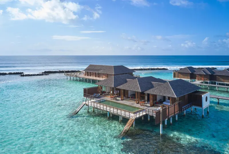 Bungalows sur pilotis au-dessus d'une eau turquoise et claire.