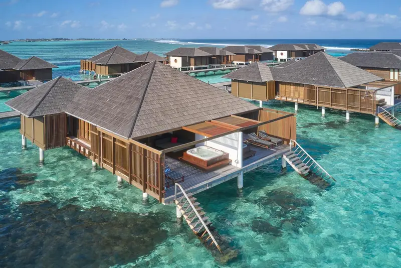 Vues aériennes de bungalows sur pilotis au-dessus d'une eau turquoise.