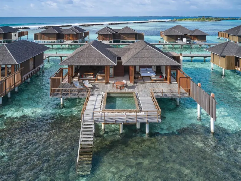 Vue aérienne de bungalows sur pilotis au-dessus d'une eau turquoise.