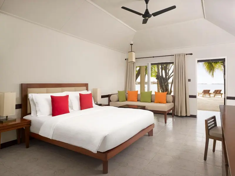 Une chambre lumineuse avec un grand lit et un coin salon donnant sur une plage.
